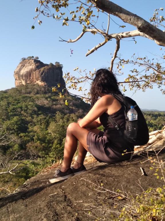 una donna seduta su una roccia con una bottiglia d'acqua di Sigiriya Lions Rest Hostel a Sigiriya