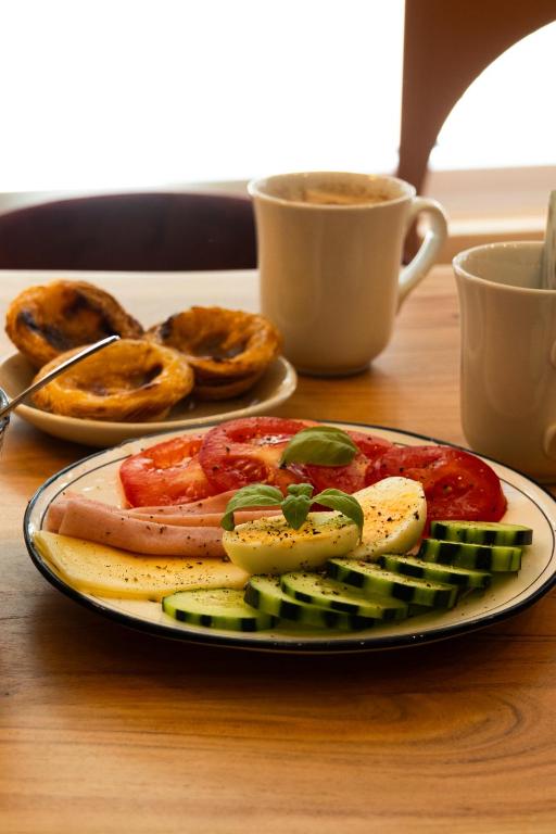 A breakfast plate of tomatoes, cucumber, fruit and pastries beside coffee.