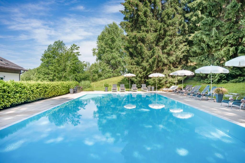 a large blue swimming pool with chairs and umbrellas at Romantik Hotel Die Gersberg Alm mit Panoramablick auf Salzburg und Outdoor Pool ab Mai in Salzburg