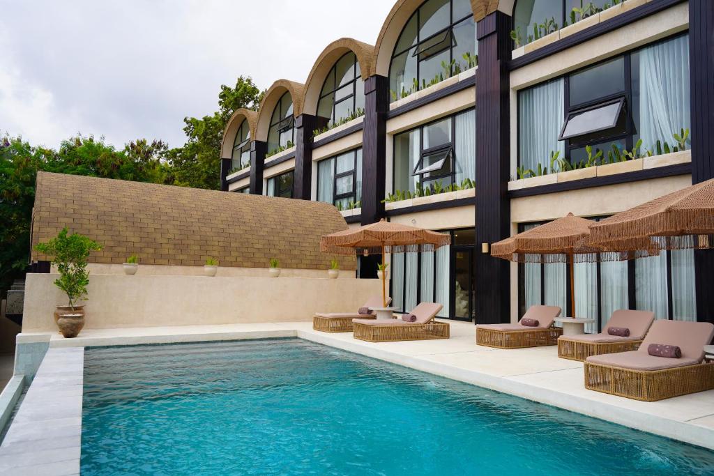 ウルワツにあるSunny Samudraの建物の隣にプール(椅子、パラソル付)