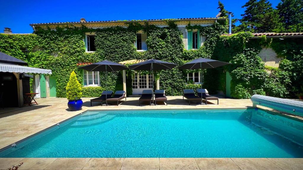 a swimming pool in front of a house with umbrellas at Le Mas Des Abeilles - Chambres d'hôtes en Drôme Provençale in La Bégude-de-Mazenc
