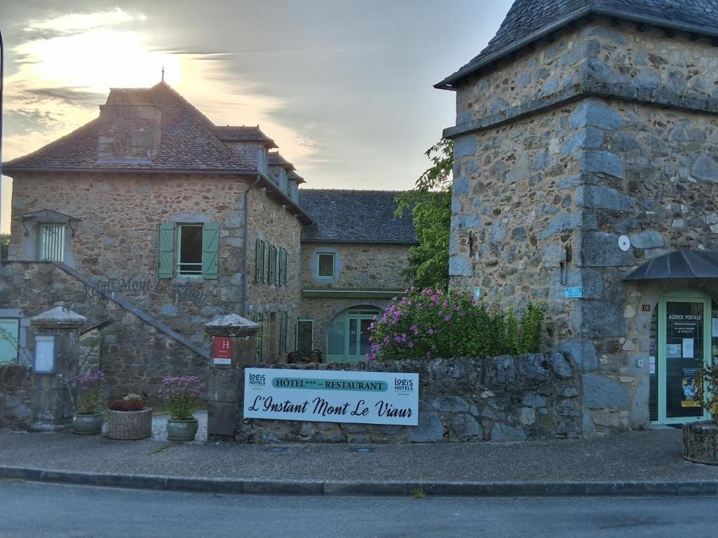 un bâtiment en pierre avec un panneau en face de celui-ci dans l'établissement Logis hôtel l'instant Mont le Viaur, à Saint-André-de-Najac