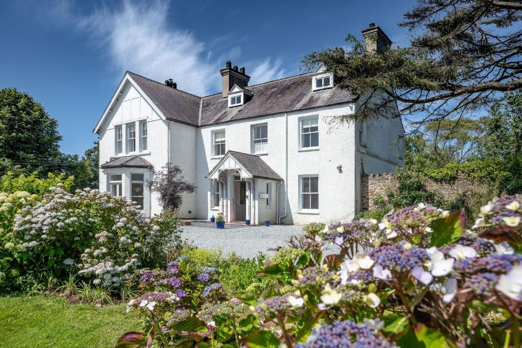 a white house with flowers in front of it at Country Retreat Sleeping 15 - Bron Menai in Newborough