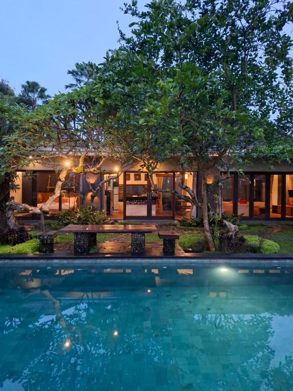 a swimming pool in front of a house with a tree at Ubud Virgin Villa in Ubud