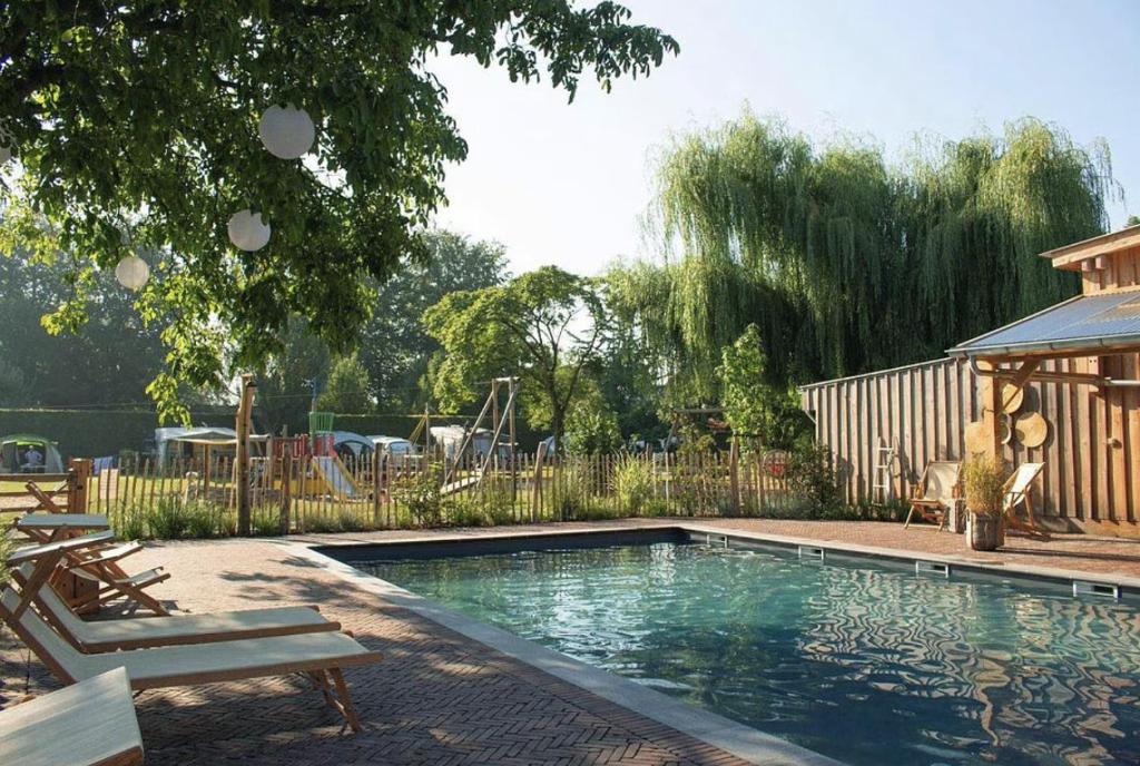 a swimming pool with two chairs and a playground at Camping Mareveld in Schimmert