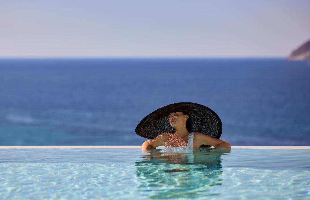 a woman in a hat sitting in a swimming pool at Hotel Milos Sea Resort in Adamantas