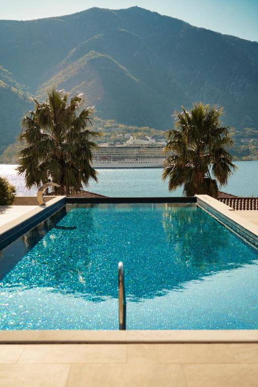 Infinity pool with mosaic deck, palm trees and ladder, overlooking a cruise ship and mountain in the distance at HUMA Kotor Bay Hotel and Villas in Kotor