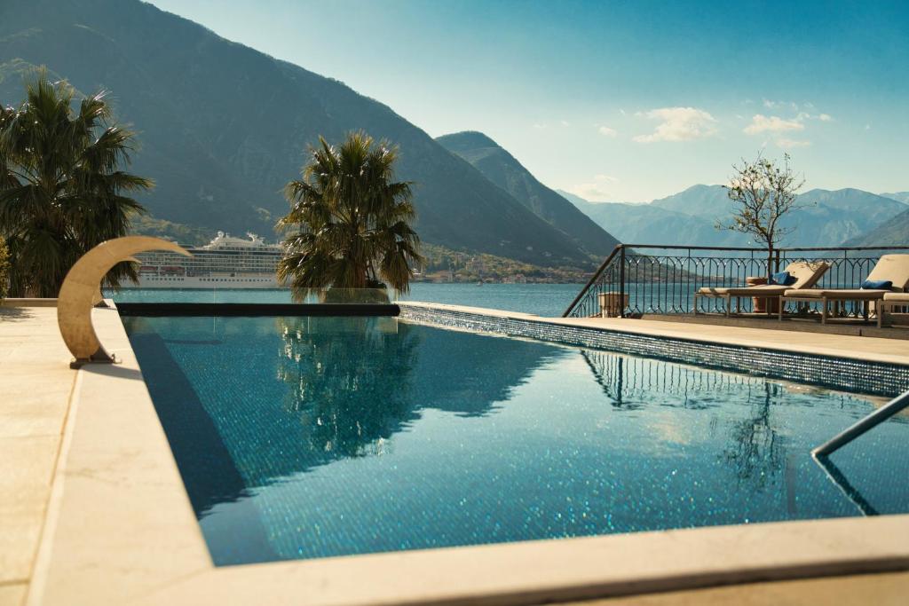 Lakefront infinity pool with mosaic tile, palm-lined deck, sun loungers and mountain views with a cruise ship on the water at HUMA Kotor Bay Hotel and Villas in Kotor