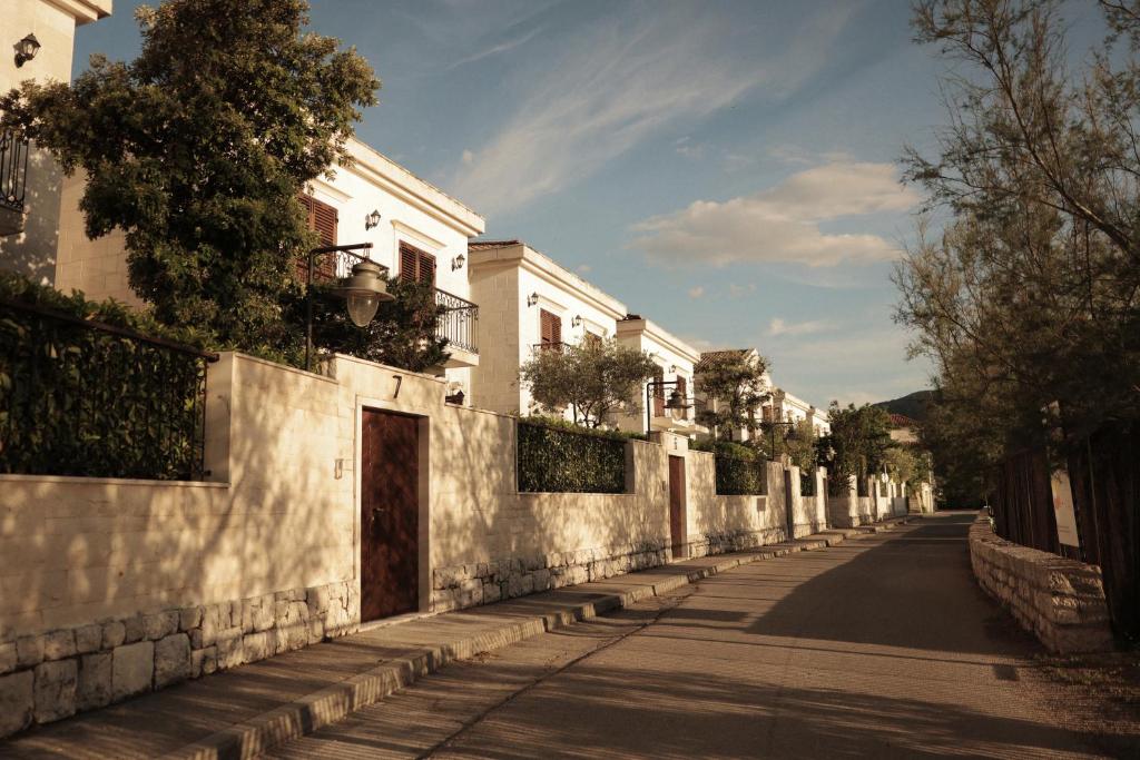 Row of white Mediterranean villas with shuttered windows, stone walls, olive trees and a paved lane with house number 7 at HUMA Kotor Bay Hotel and Villas in Kotor