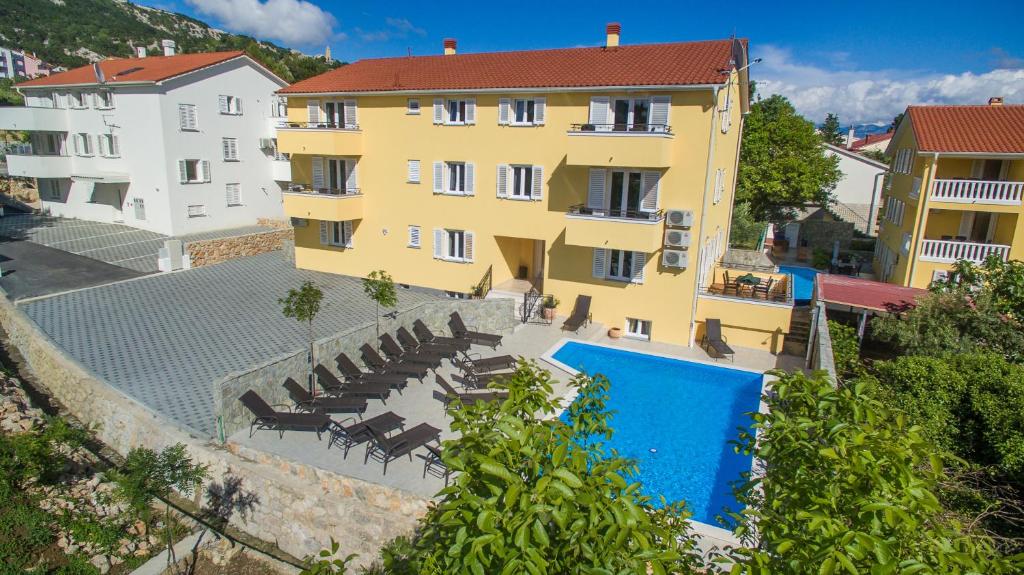 a large yellow building with a swimming pool and chairs at Apartments Gorica 2 in Baška