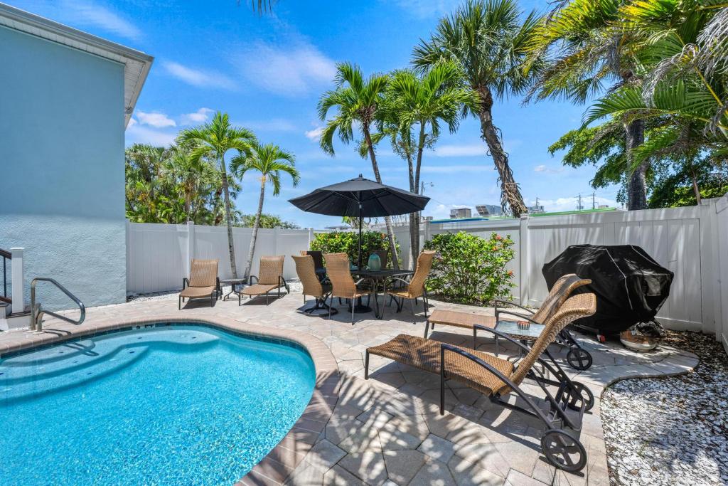 a patio with a swimming pool and chairs and an umbrella at Tidal Wave - In Siesta Key Village, Pet Friendly, Private Pool! in Siesta Key