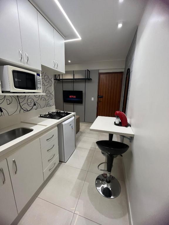 a kitchen with white cabinets and a table and a stool at Brasília Kit 115 Sudoeste in Brasília