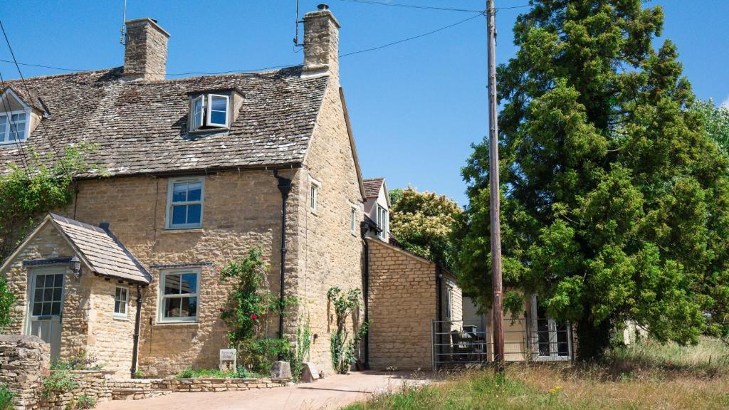 una vieja casa de ladrillo con un árbol delante en Inglenook Cottage, en Charlbury