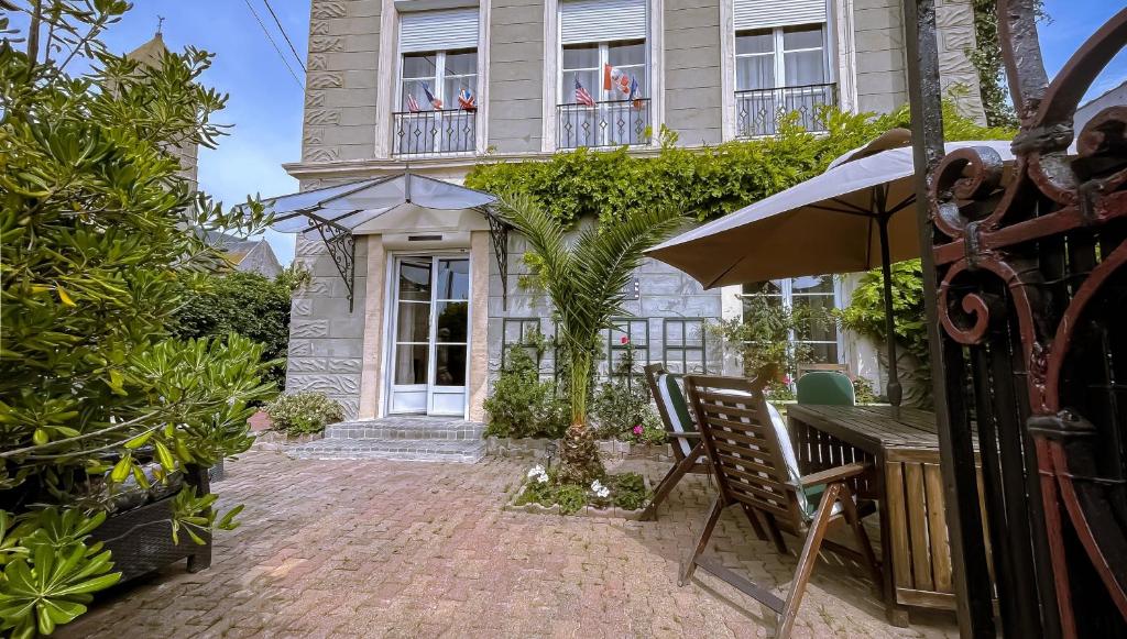 a patio with a table and an umbrella in front of a building at Grande Maison Historique Confortable Climatisée in Ver-sur-Mer