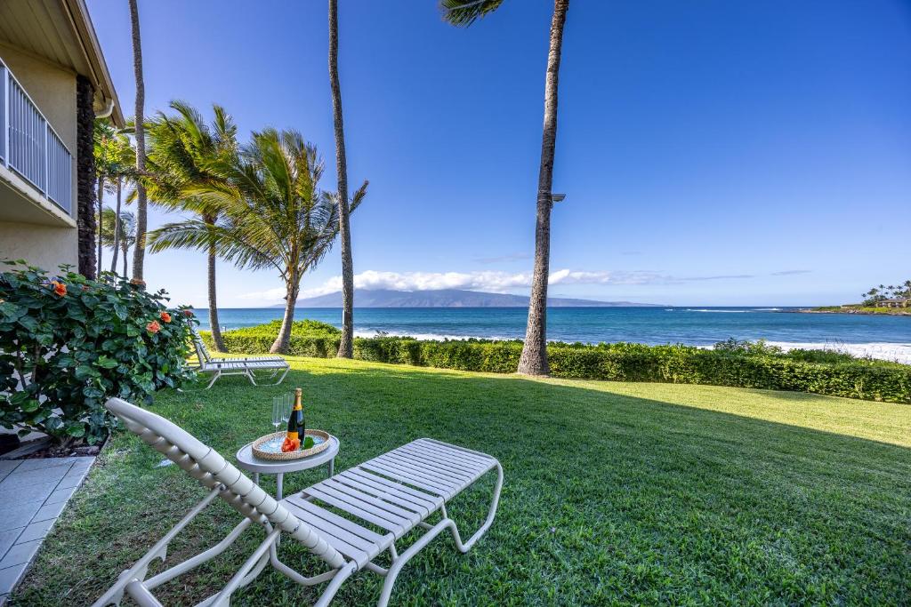 a lawn with a chair and a table with a bottle of wine at Napili Shores - Ocean Front Ground Floor in Kahana