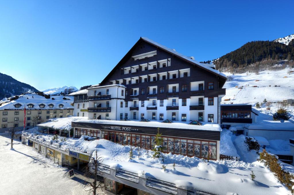 un grand bâtiment dans la neige devant une montagne dans l'établissement Hotel Post, à Sankt Anton am Arlberg