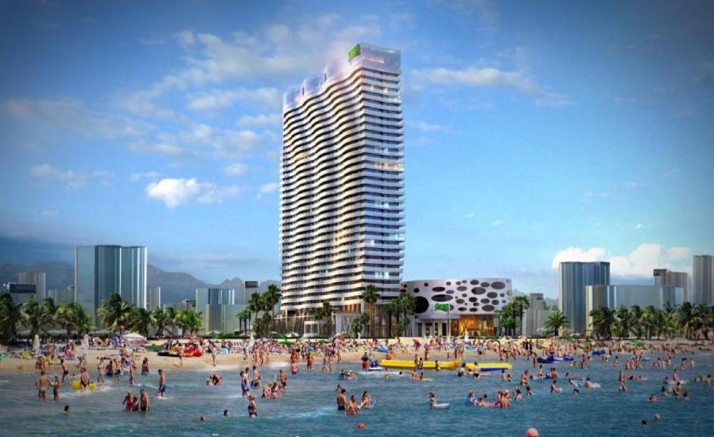 un grupo de personas en una playa con un edificio alto en White Sail Apartments, en Batumi