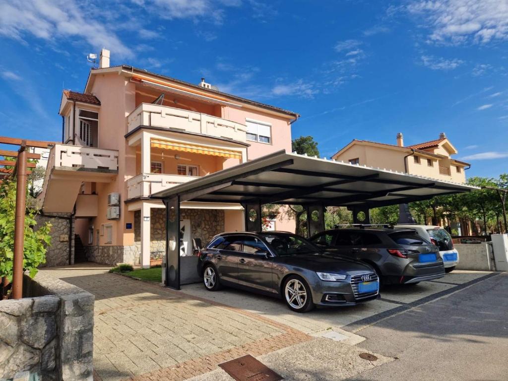 dwa samochody zaparkowane pod garażem przed domem w obiekcie Apartman Ruza w Krku