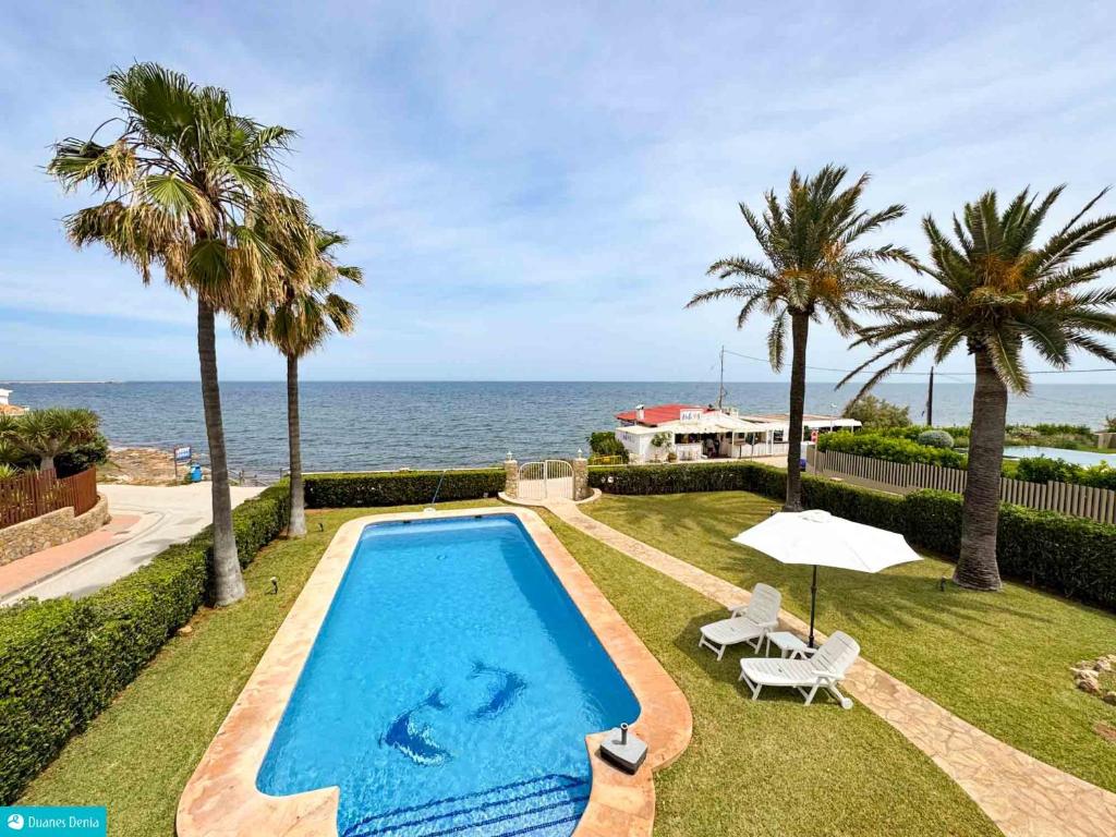 een zwembad met palmbomen en de oceaan bij casa frente el mar in Denia
