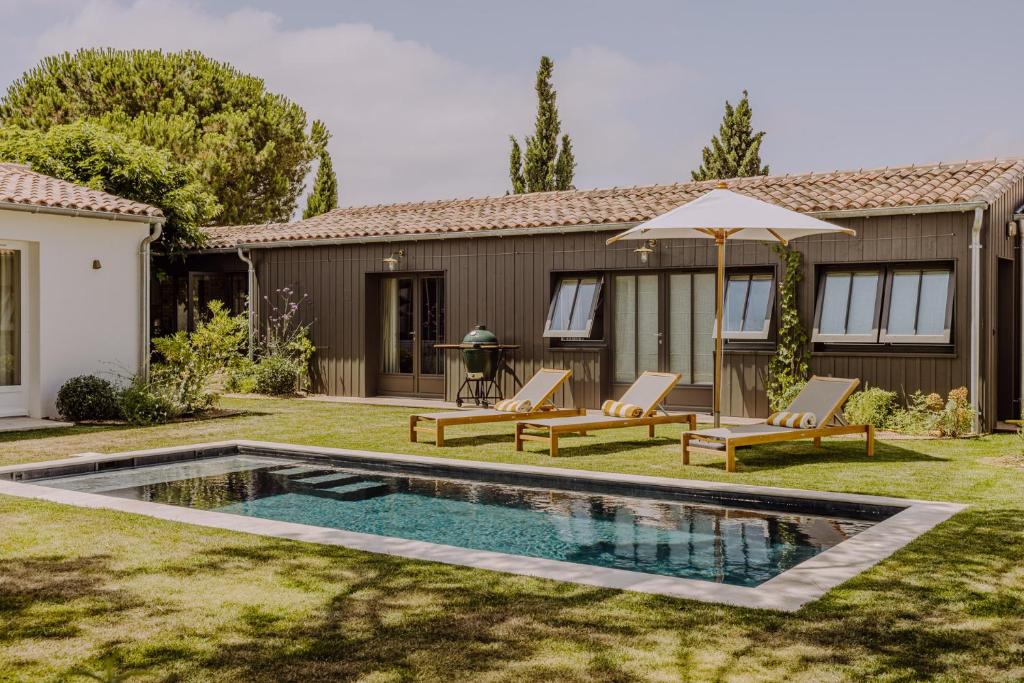 een achtertuin met een zwembad met 2 stoelen en een parasol bij Villa Rhétaise - Loix in Loix