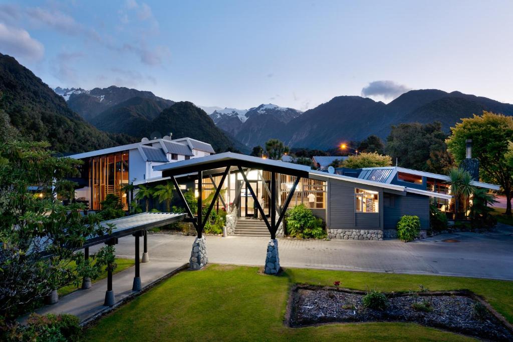
a large white house with a patio and trees at Scenic Hotel Franz Josef Glacier in Franz Josef

