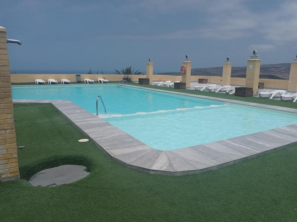 a large swimming pool with green grass and chairs at Lucas beach in Mogán