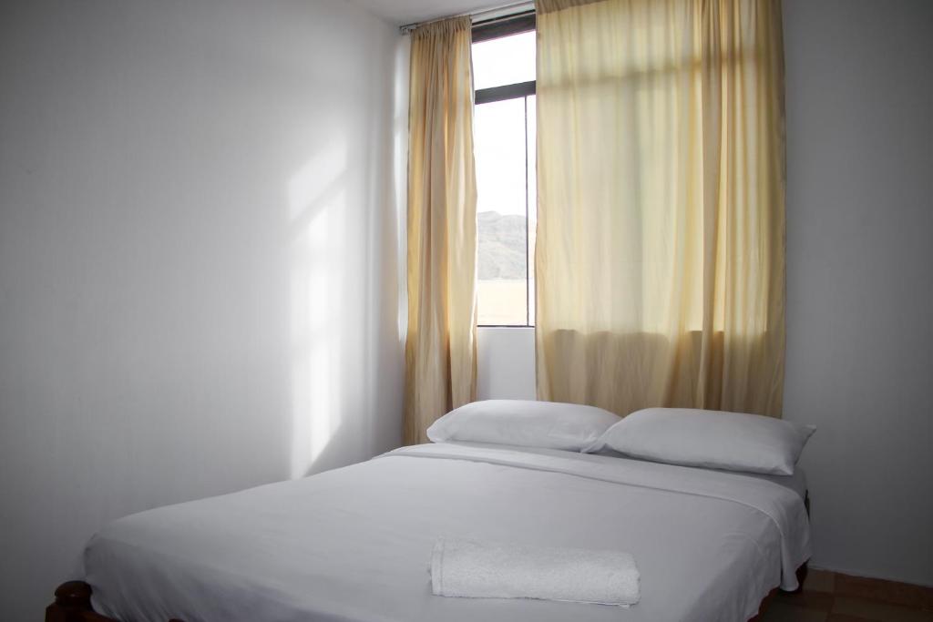 a bedroom with a white bed with a window at Hospedaje Los Organos in Los Órganos