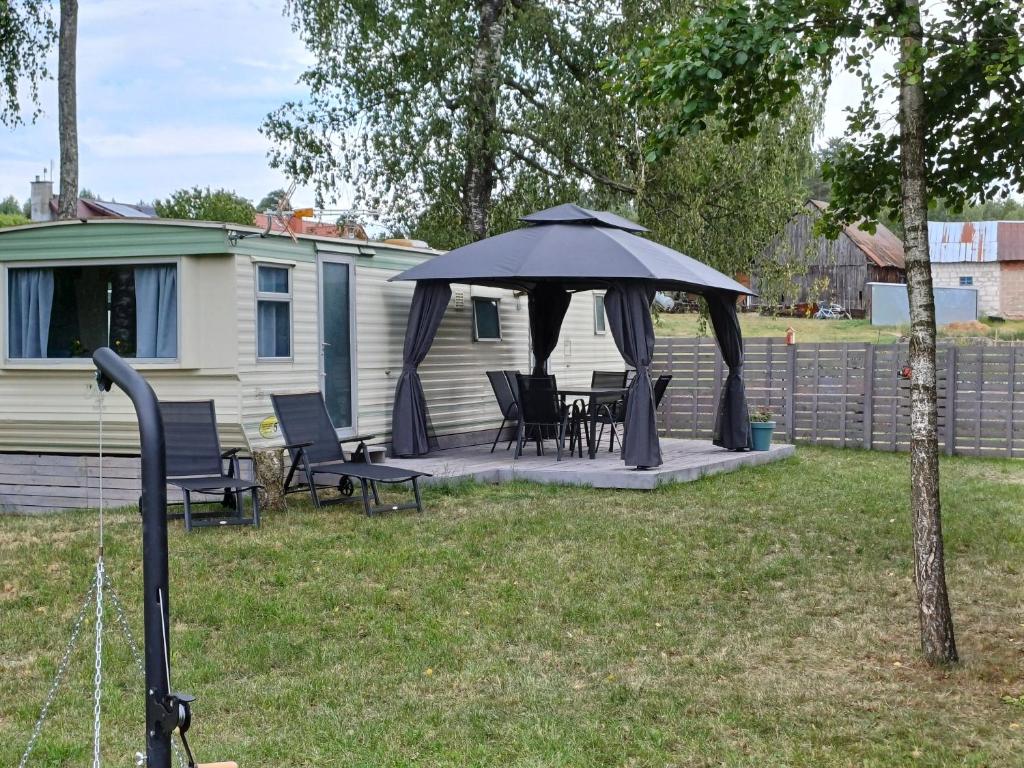 a patio with chairs and an umbrella in front of a caravan at Domek holenderdki ZaCisze 2 in Augustów