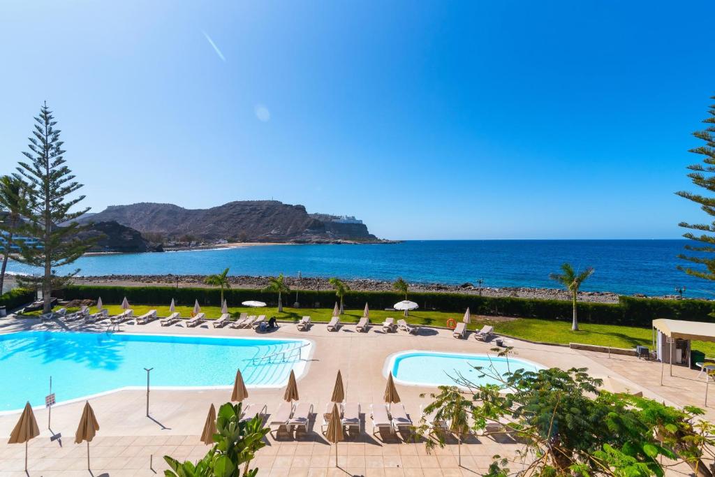 a pool with chairs and the ocean in the background at Paradise Playa del Cura in Las Palmas de Gran Canaria