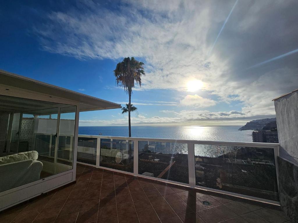 a balcony with a view of the ocean and a palm tree at Sunset Balcony with Ocean Views and pool access in Mogán