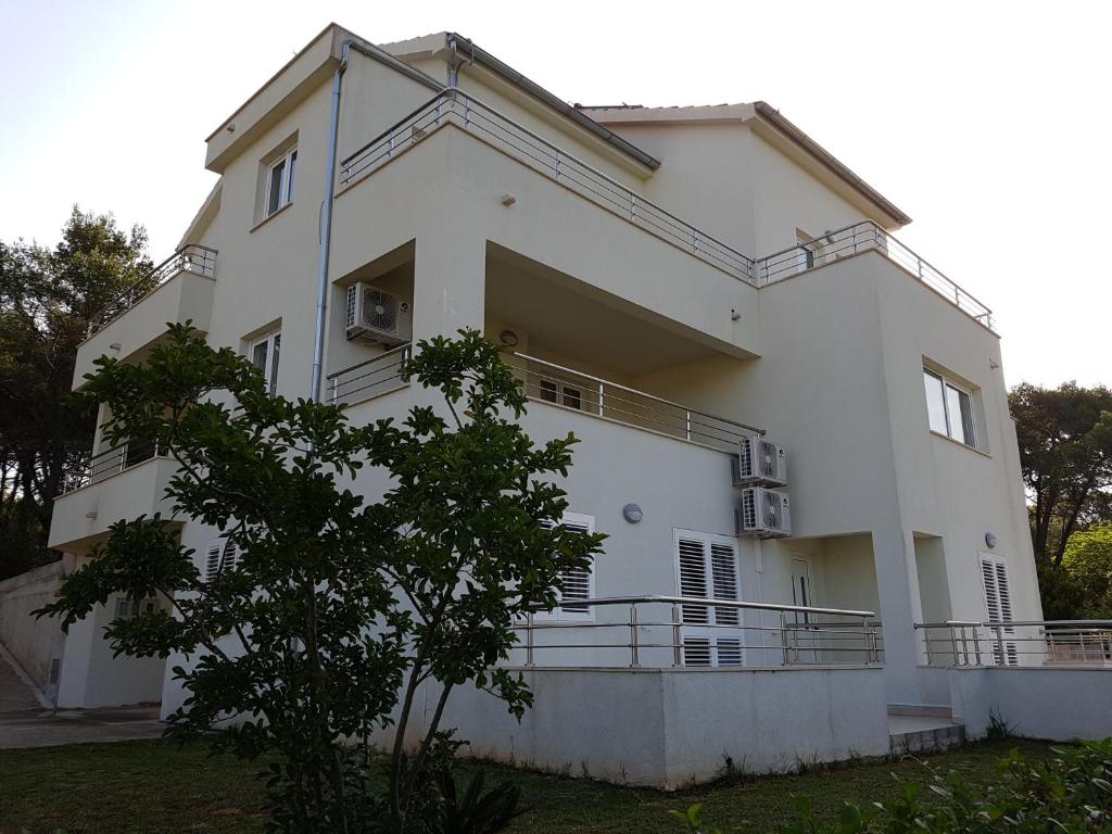 a white house with a tree in front of it at Apartments Villa Maslinica in Vrboska