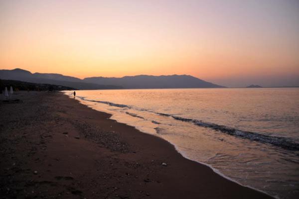 a beach at sunset with a person walking on the shore at Elli Studios & Apartments in Marathokampos