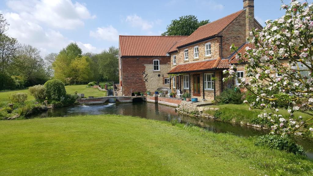 une maison en briques avec une rivière devant elle dans l'établissement Watermill Farm Cottages, à Metheringham