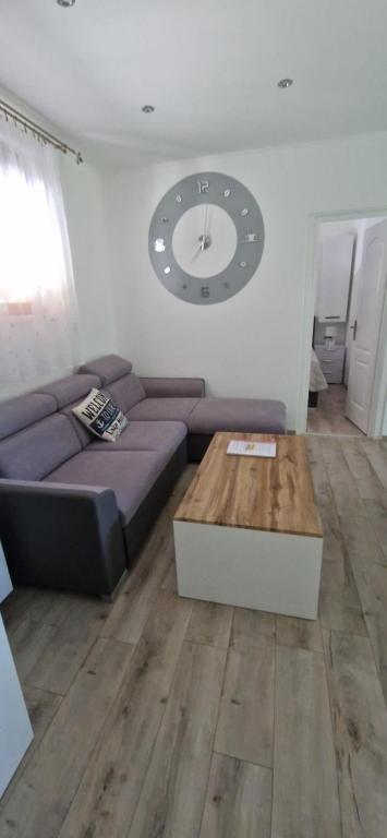 een woonkamer met een bank en een klok aan de muur bij Rozmaring Apartman Csopak in Csopak