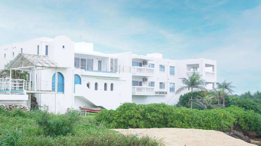 a large white building on the beach with trees at ブルーシャローズ 恩納村リゾート in Ukaji