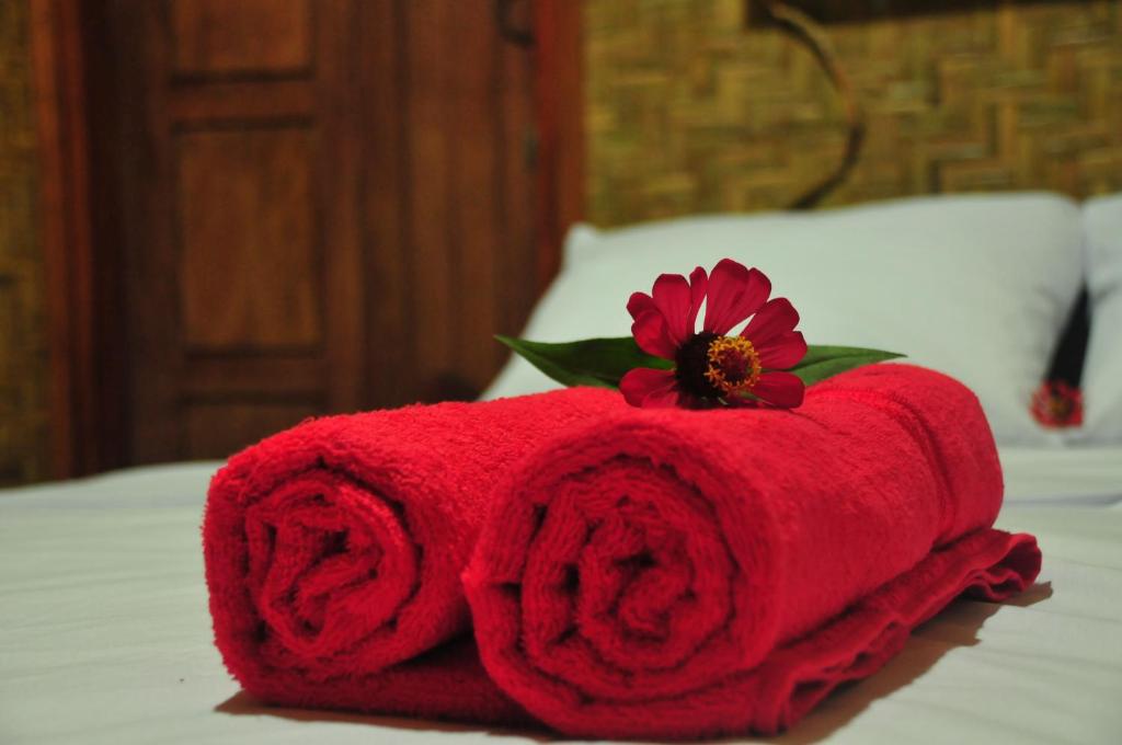 a red towel with a flower on top of a bed at Green Haven Homestay in Tetebatu