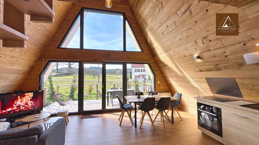 a living room with a large window and a table and chairs at Les Atypiques Chalets in Barbey-Séroux