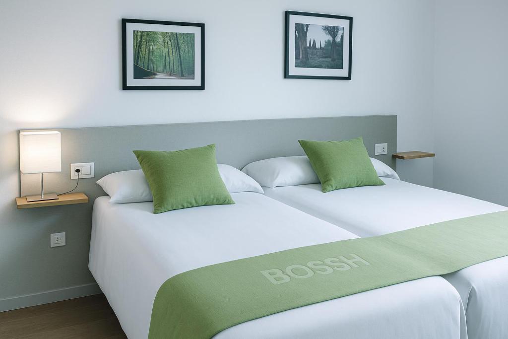 a bedroom with a bed with white sheets and green pillows at Apartamentos Turísticos Cancelas by Bossh Hotels in Santiago de Compostela