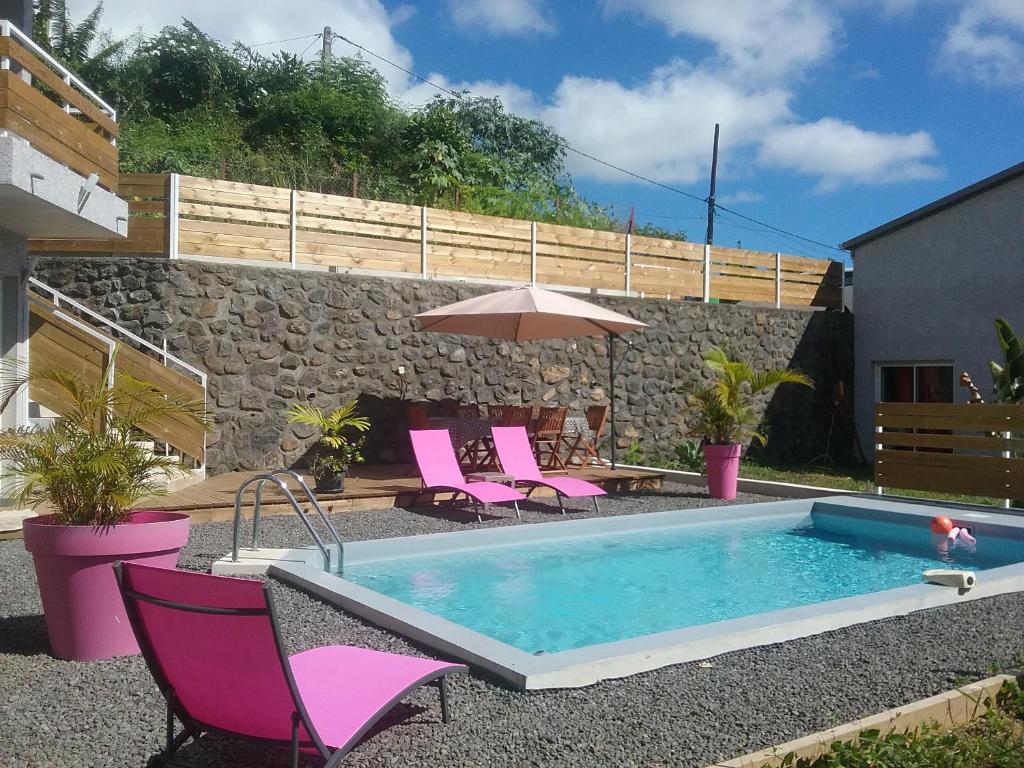 einen Pool mit rosa Stühlen und einem Sonnenschirm in der Unterkunft Les Canneliers in Saint-Leu