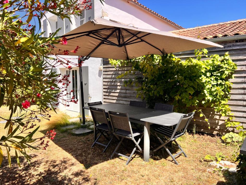 einen Tisch und Stühle unter einem Regenschirm im Hof in der Unterkunft Maison LA BEURELIÈRE proche Plage in Sainte-Marie-de-Ré