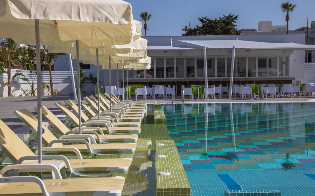 a pool with chairs and umbrellas next to a building at Nicholas Color Hotel in Ayia Napa