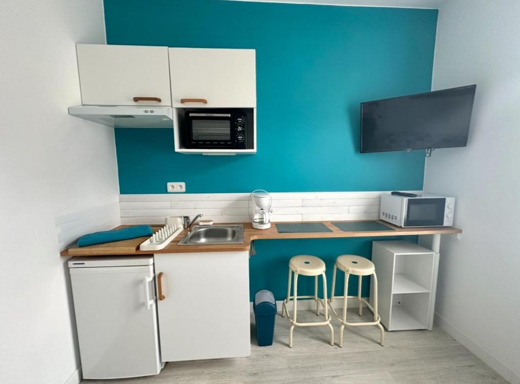 Elle comprend une petite cuisine avec des placards blancs et un mur bleu. dans l'établissement Studio BLEU - à 100 m de la plage de Berck, à Berck-sur-Mer