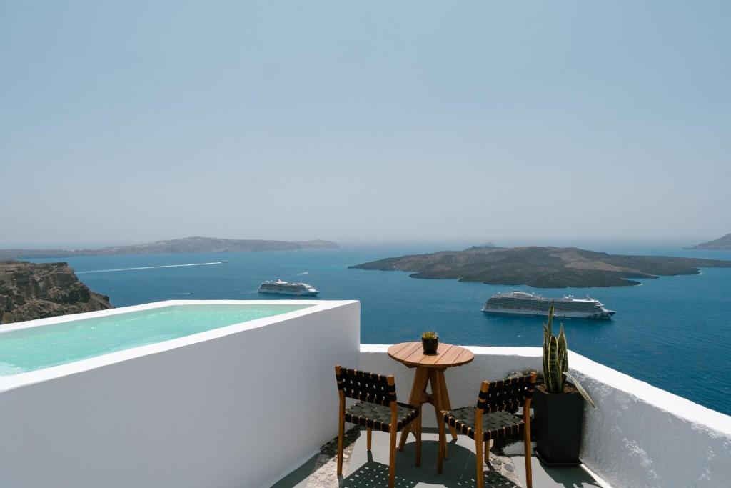a small table and chairs on a balcony overlooking the ocean at Anemos Fira Caldera View in Fira
