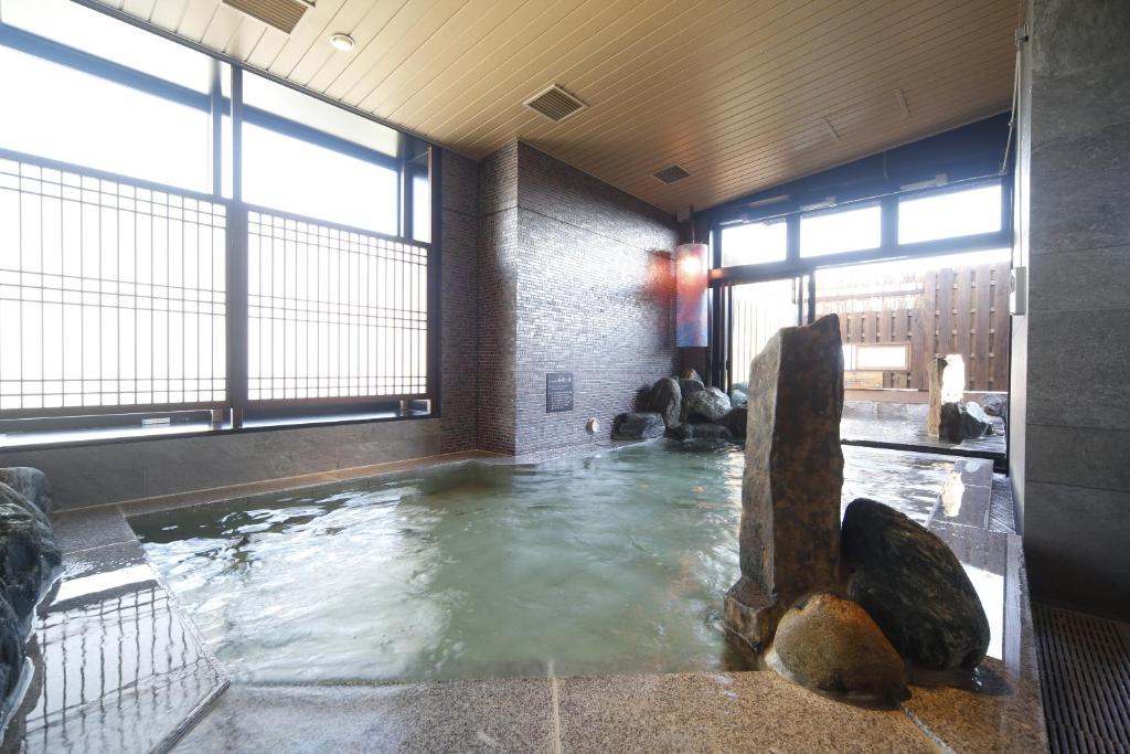 Una piscina de agua con rocas en una habitación con ventanas en Natural Hot Spring Shoun no Yu Dormy Inn Kofu Marunouchi, en Kofu