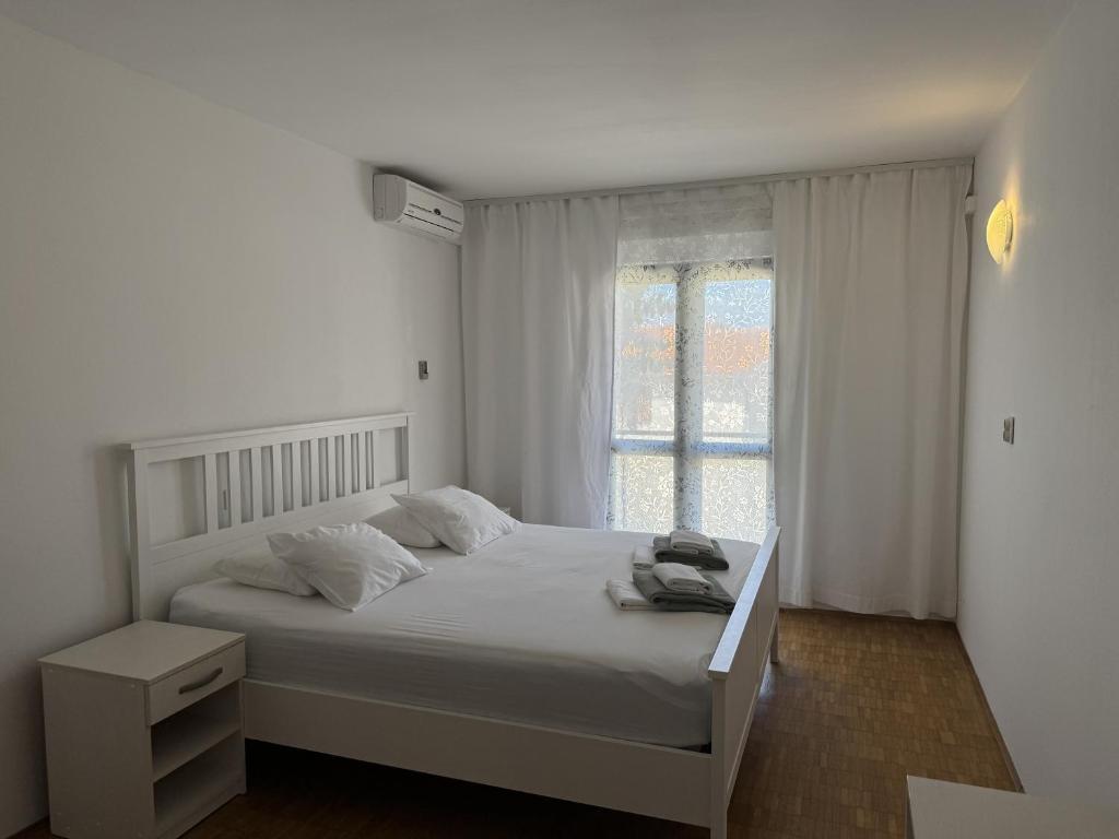 a white bedroom with a bed and a window at Apartment Retro in Podgora