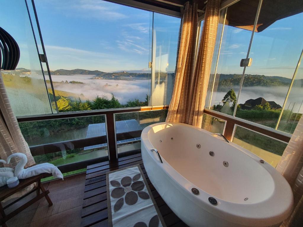 a bathroom with a bath tub in front of a window at Chalé 3 com Hidro Acima das Nuvens in Campos do Jordão