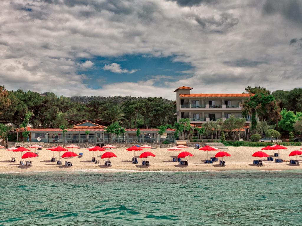 佩夫卡里的住宿－Hotel Akti，海滩上设有红色遮阳伞和椅子,还有一座建筑