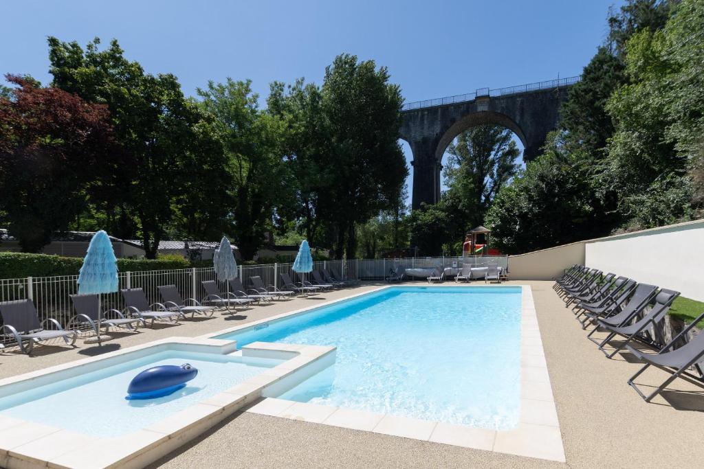 a swimming pool with chairs and a bridge in the background at Les Rives d’Auzon confort 8 pers in Lavilledieu