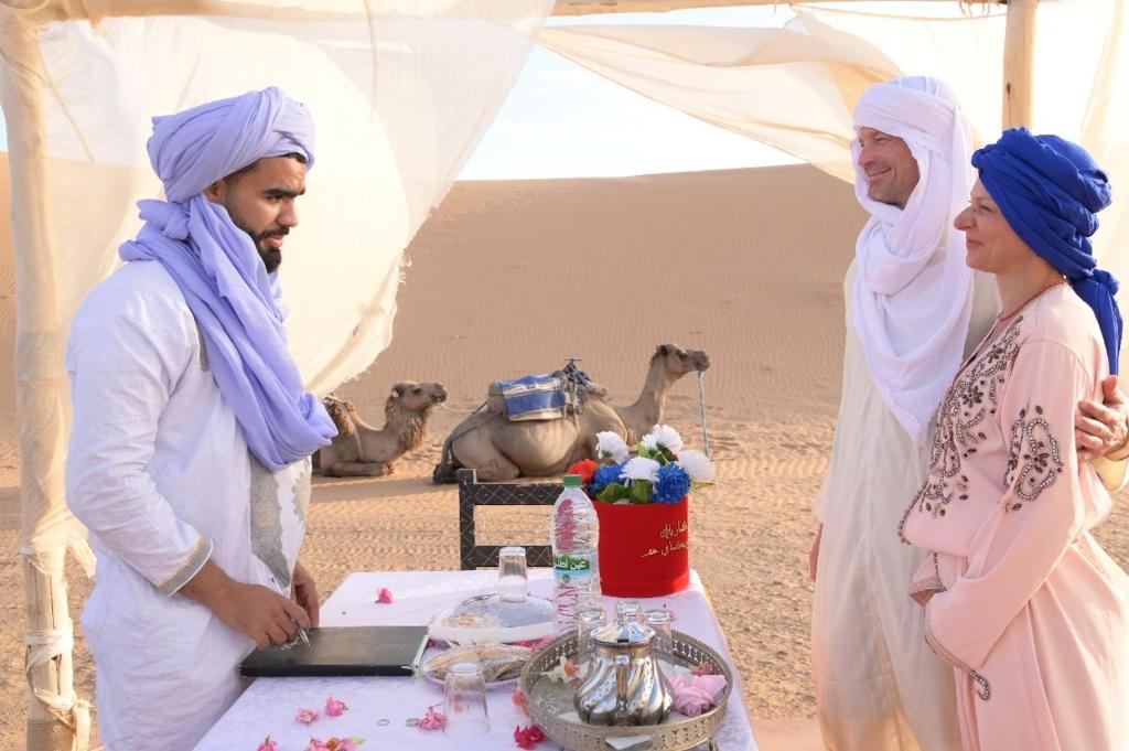 Un hombre y una mujer de pie junto a una mesa en el desierto. en Luxury camps merzouga, en Merzouga