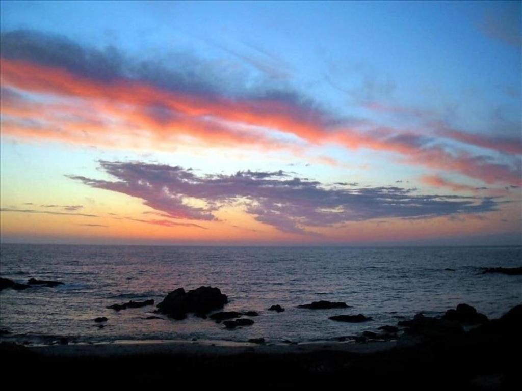 a sunset over the ocean with rocks in the water at 3976 Mirka's Beach House home in Pacific Grove
